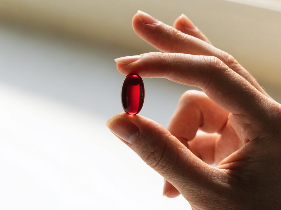 A single deep red astaxanthin softgel held up to the light